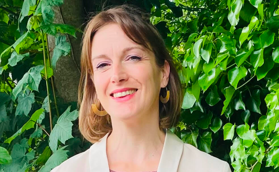 Portrait of a smiling individual standing in front of a lush green leafy background