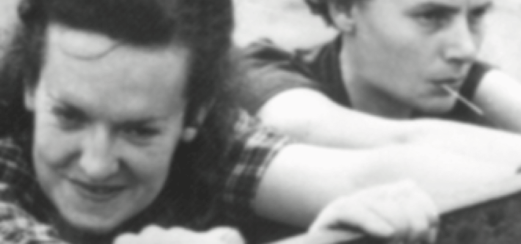 Black-and-white portrait of a smiling individual, with another person in the background